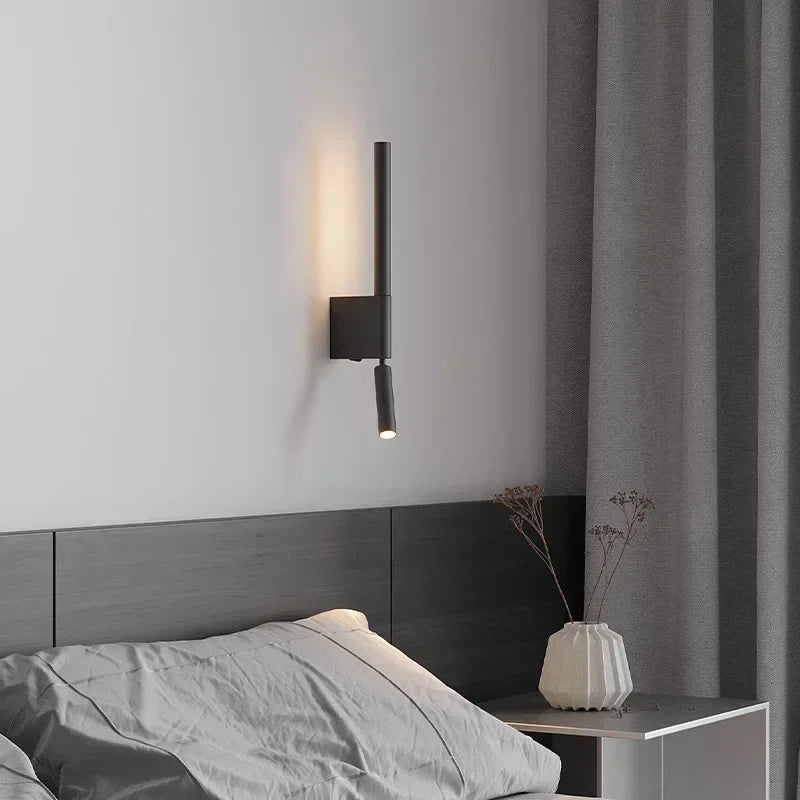 A black adjustable LED wall sconce mounted above a dark headboard in a bedroom setting.