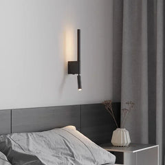 A black adjustable LED wall sconce mounted above a dark headboard in a bedroom setting.