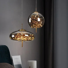 Two glass pendant lights with gold accents, filled with warm LED lights, hanging against a dark wall.