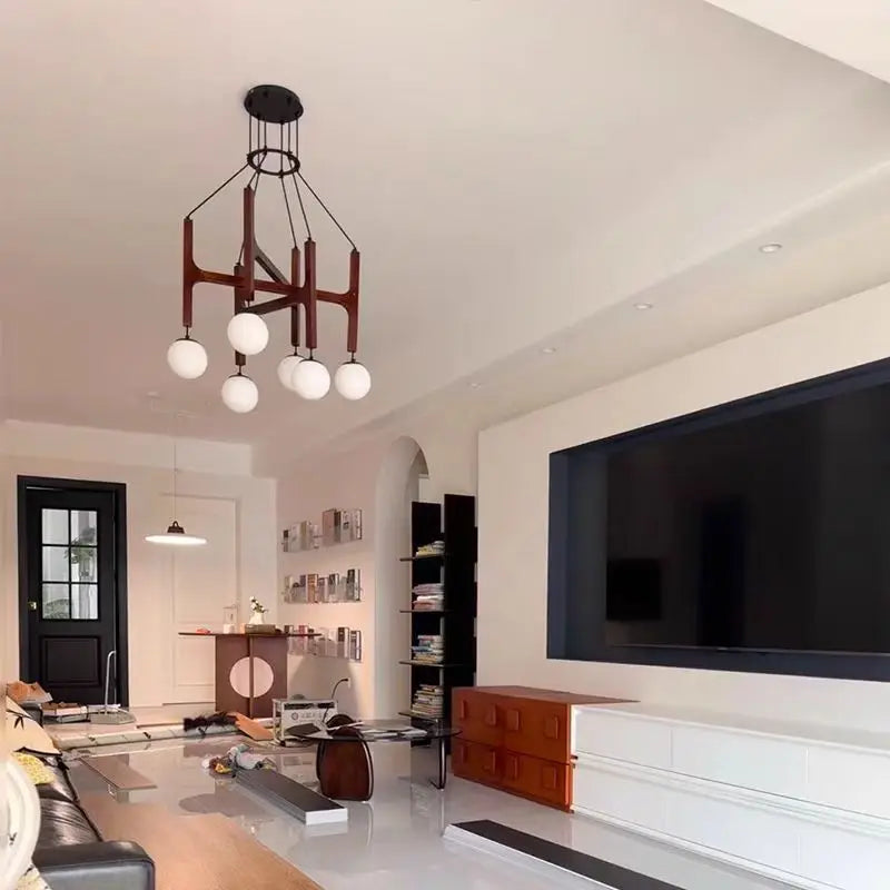 A living room featuring a dark wood and glass multi-arm chandelier above a large television and white furniture.