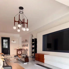 A living room featuring a dark wood and glass multi-arm chandelier above a large television and white furniture.