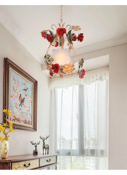 A gold floral pendant light with red rose accents illuminating a room, mounted above a wooden dresser with decorative items.
