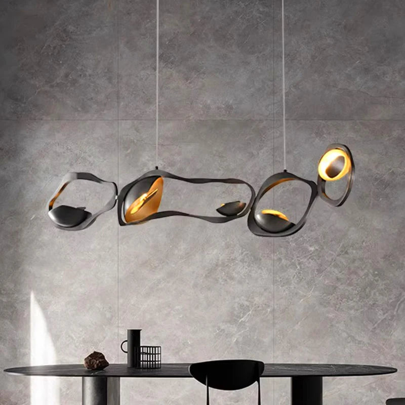 Modern chandelier with gold accents hanging above a dining table against a gray wall.