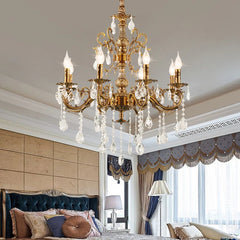 A coppery multi-arm crystal chandelier illuminated above a bed in a bedroom setting.