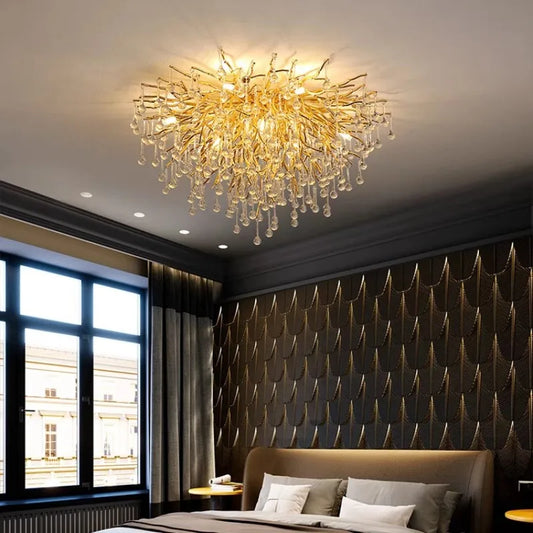 A round, gold crystal chandelier with a branch-like design and teardrop crystals hanging above a bed.