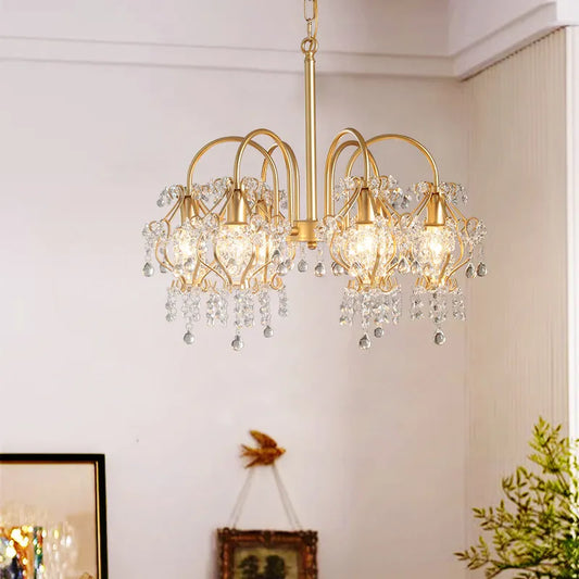 A gold-finished chandelier with multiple arms, adorned with cascading clear teardrop and faceted crystals, suspended from a chain against a white ceiling.