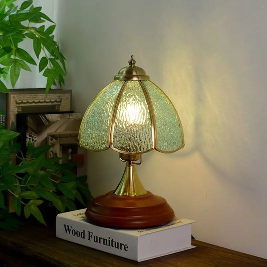 Close-up of a brass table lamp with a textured green glass shade, showcasing its metallic accents and wooden base.