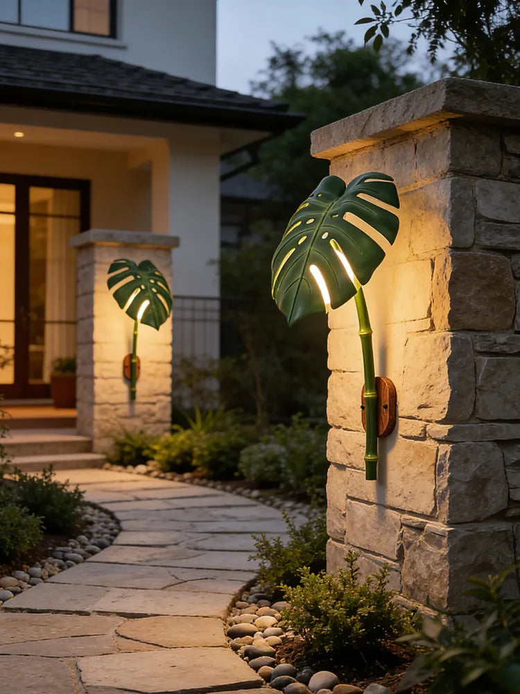 Green leaf bamboo wall sconces illuminating a stone pathway and exterior wall of a house at dusk.