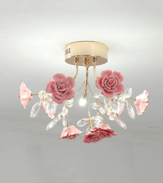 A close-up view of a pink ceramic rose and crystal embellishments on a gold flush mount ceiling light.