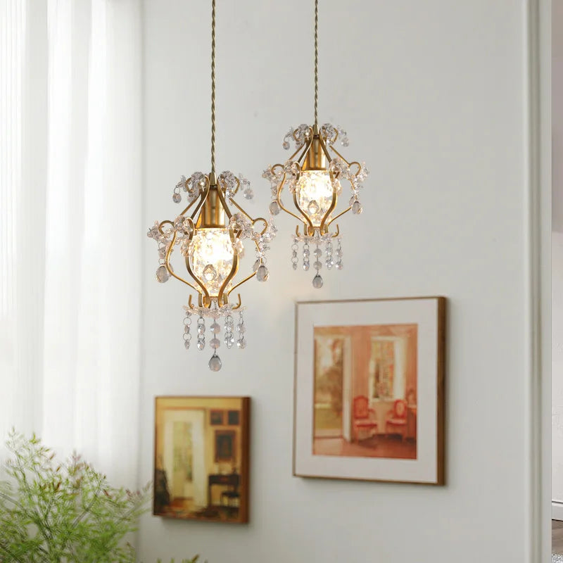 Two gold pendant lights with crystal accents hanging on a wall with framed pictures.