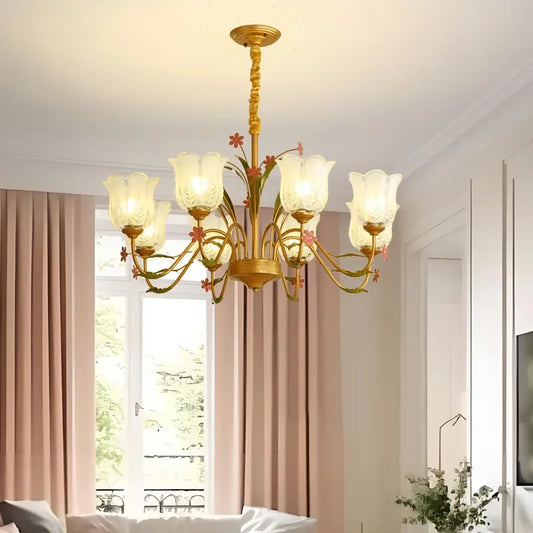 Gold floral chandelier illuminated in a room with pink curtains and a sofa.