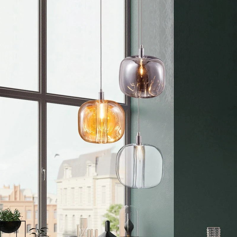 A trio of crystal ball pendant lights in amber, smoke gray, and clear, near a large window with a city view.