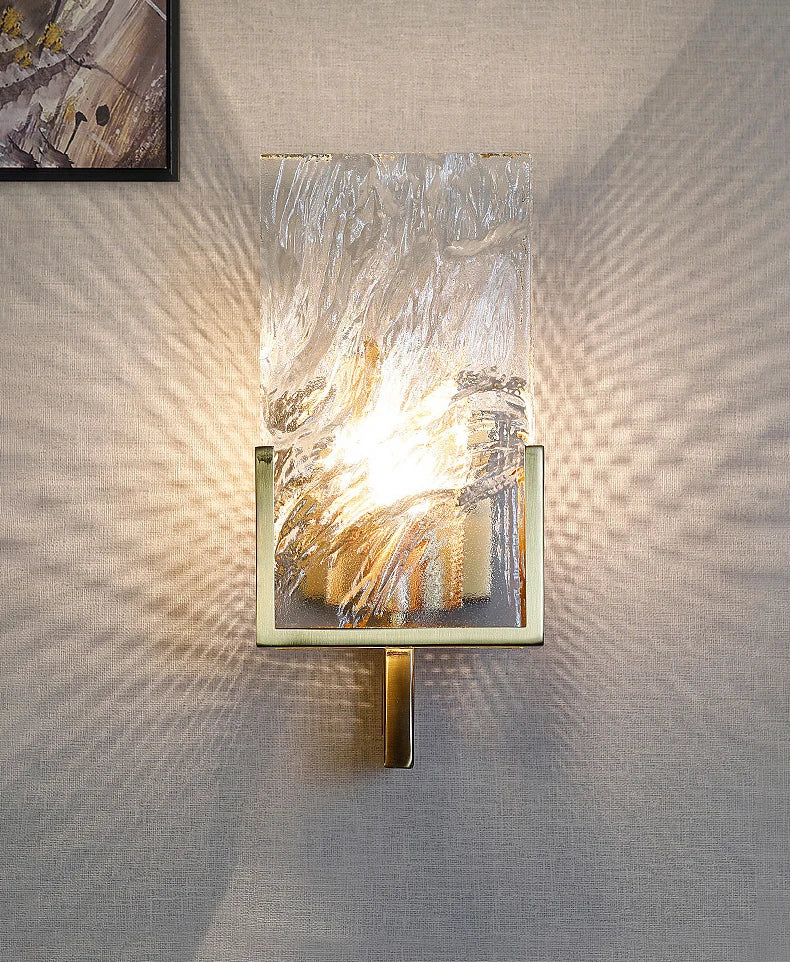 Wall-mounted light fixture with textured glass shade on a textured wall.