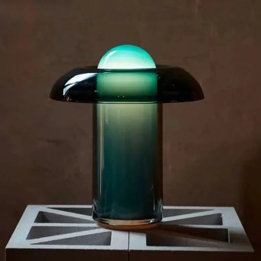 A single glass mushroom table lamp with a gradient shade on a concrete block against a dark background.