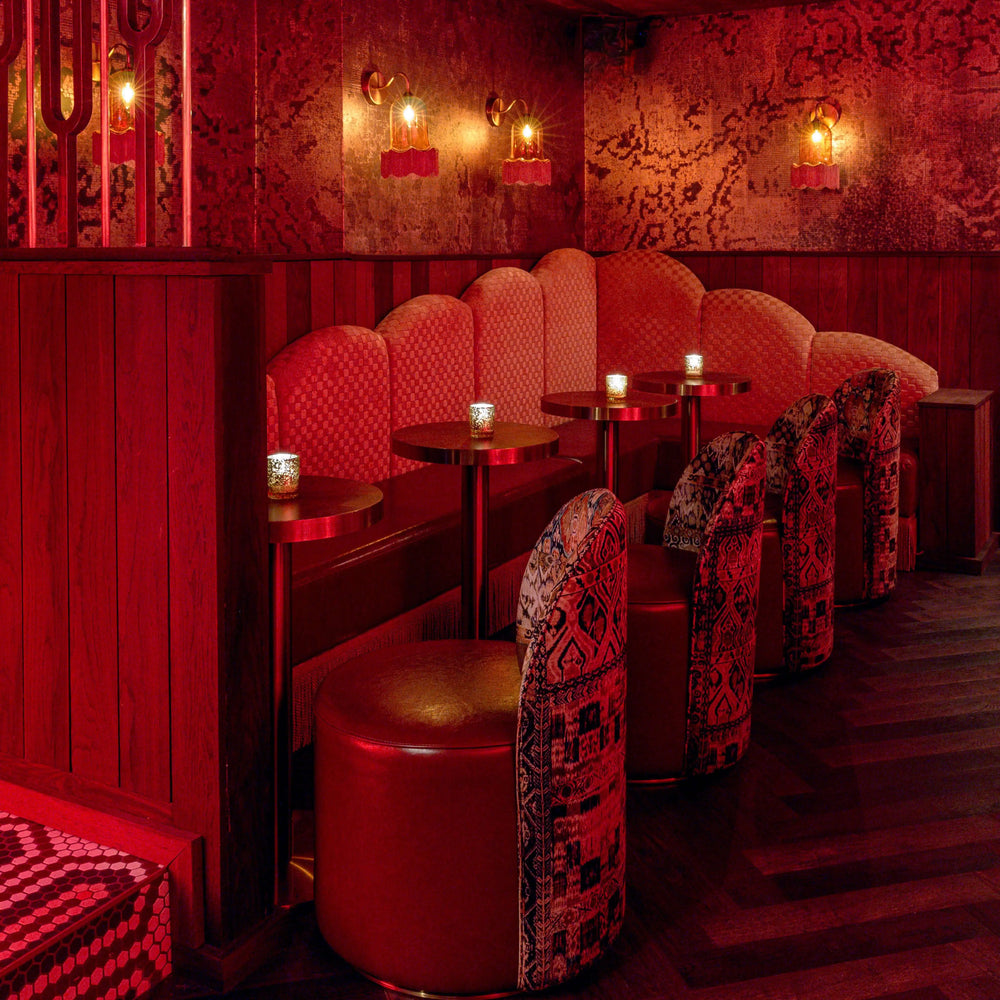 A dimly lit lounge area with multiple wall sconces featuring bell-shaped glass shades and tassel accents, mounted on a textured red wall.