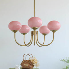 A low-angle view of a gold chandelier with five pink globe-shaped glass shades, with a woven basket in the foreground.
