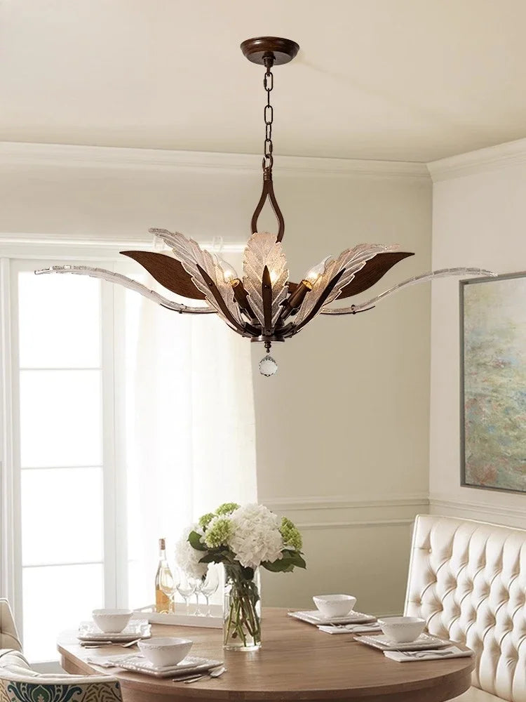 A bronze chandelier with glass leaf shades and crystal accents hanging above a dining table set for a meal.