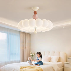 A young girl sitting on a bed, playing with a teddy bear, under a pink cloud flush mount ceiling light.