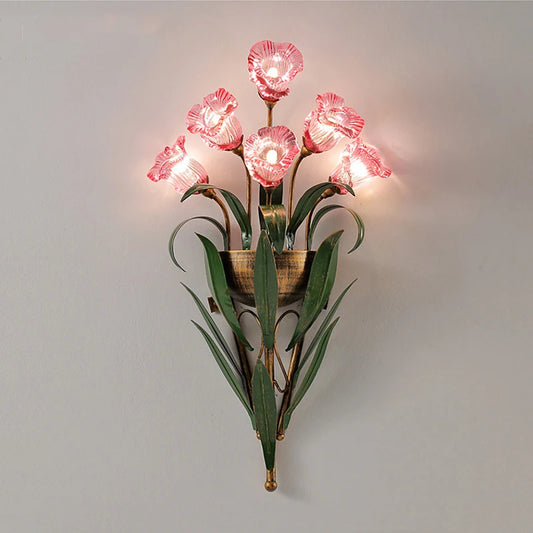 Pink floral wall sconce with clear glass flower shades and green leaf accents against a white wall.