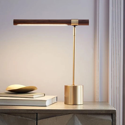 Brass and wood LED desk lamp with the light on, placed on a nightstand next to books and a decorative bowl.