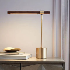 Brass and wood LED desk lamp with the light on, placed on a nightstand next to books and a decorative bowl.