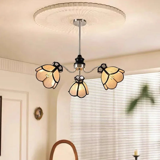 A polished chrome chandelier with three light beige, petal-shaped shades arranged in a floral pattern.