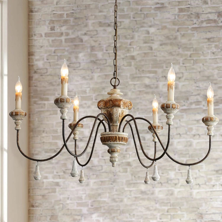 Close-up of a distressed wood and iron candle chandelier against a brick wall.
