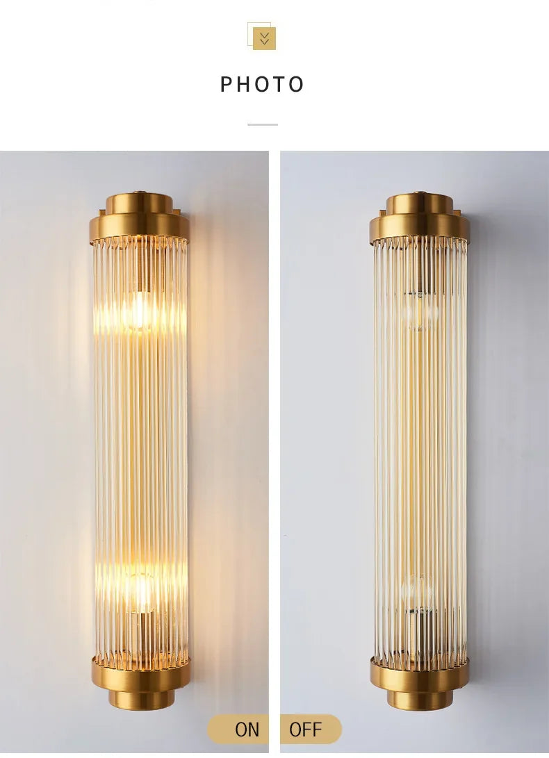 Two wall lights with gold fixtures and glass cylindrical shades, one on and one off, on a light gray background.