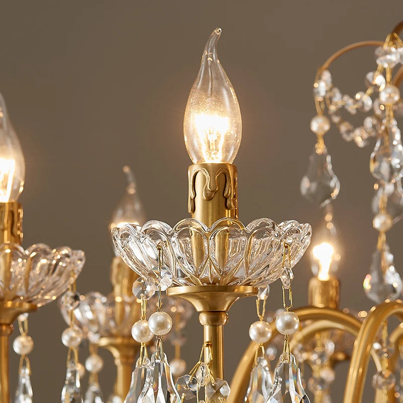 A close-up of a single candle-style light bulb on the gold chandelier, set within a decorative crystal holder.