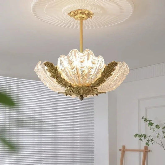 A transparent shell-shaped glass pendant light with gold leaf accents hanging from a decorative ceiling medallion.