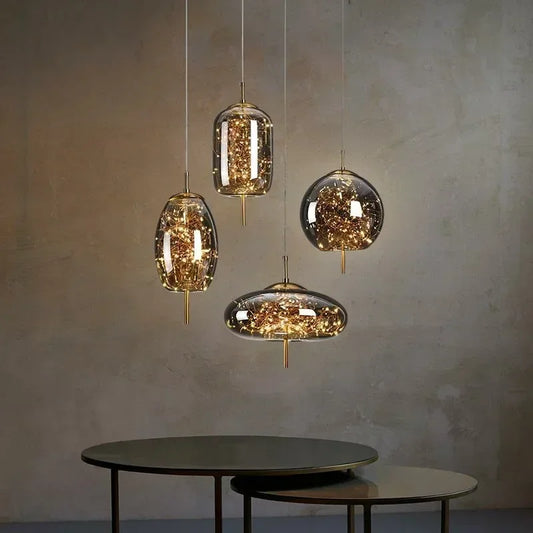 A collection of four glass pendant lights of various shapes, all containing warm LED lights and gold accents, displayed in a room setting.