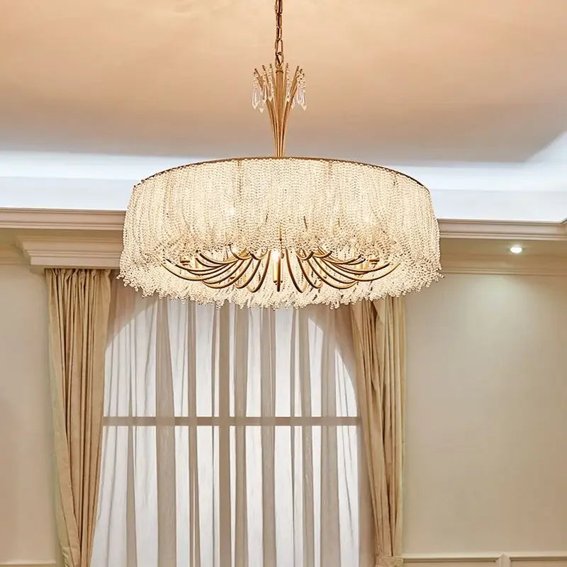 Gold crystal waterfall chandelier suspended in a room with sheer curtains in the background.