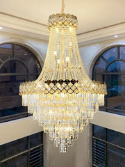 A large gold chandelier with cascading crystal accents, installed in a high-ceilinged room with arched windows.