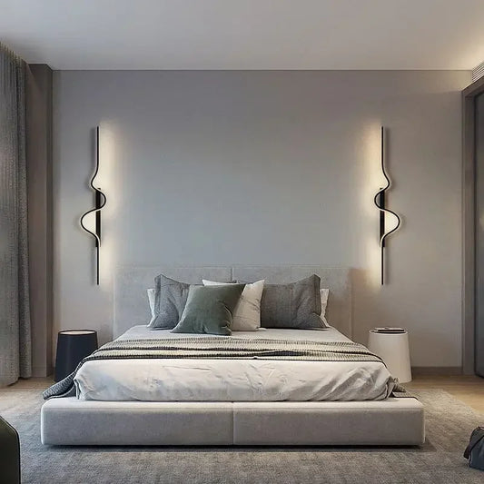 Two modern gold wall sconces with wavy designs flanking a bed in a minimalist bedroom.