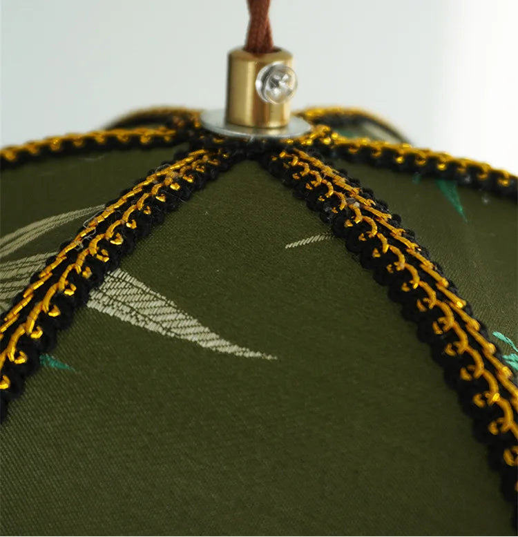 Close-up of a green fabric item with gold trim and a decorative button on a white background