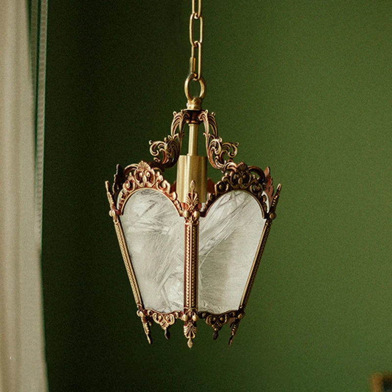A polished copper pendant light with ornate detailing and frosted glass panels, hanging against a green background.