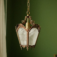 A polished copper pendant light with ornate detailing and frosted glass panels, hanging against a green background.