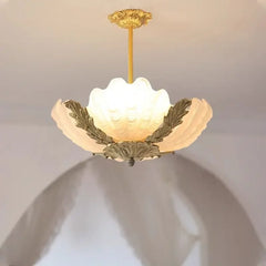 A white shell-shaped glass pendant light with polished gold leaf accents, casting a warm glow.