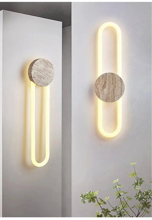 A modern wall sconce with a circular stone accent and a U-shaped yellow LED light, mounted on a white wall.