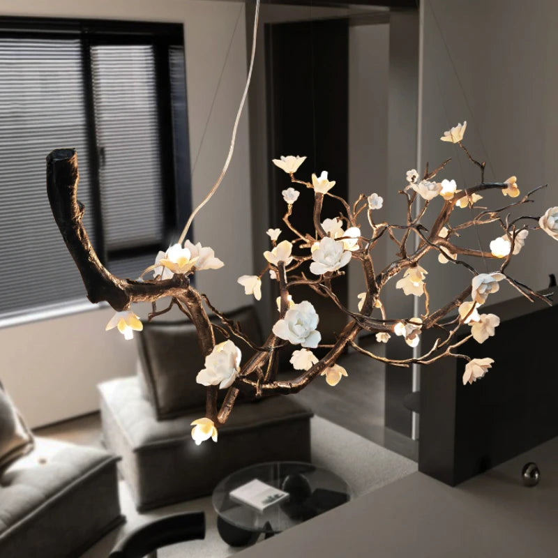 An angled shot of a unique copper chandelier with a natural branch and flower motif, emitting a warm glow in a softly lit interior space.