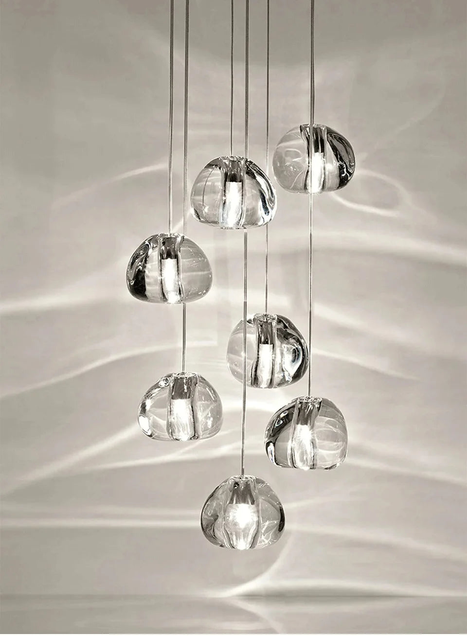 A cluster of clear crystal ball pendant lights hanging in a cascade, casting light patterns on the wall.