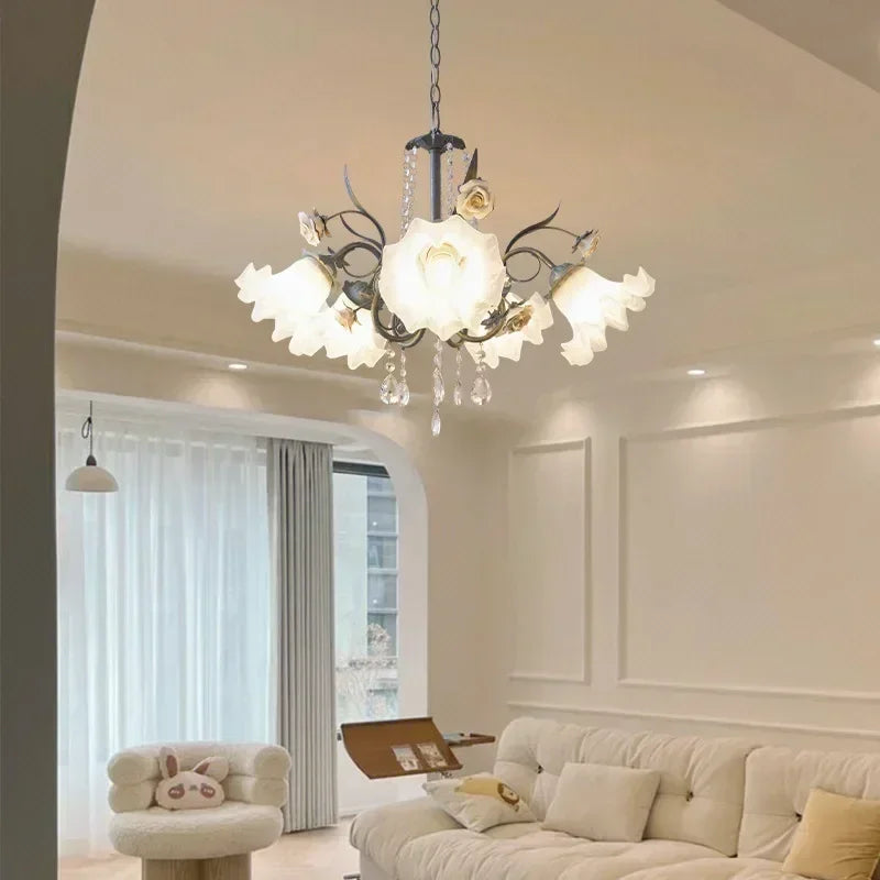 Close-up of a dark-finish floral chandelier with white ceramic roses and crystal droplets, illuminating a white sofa area.