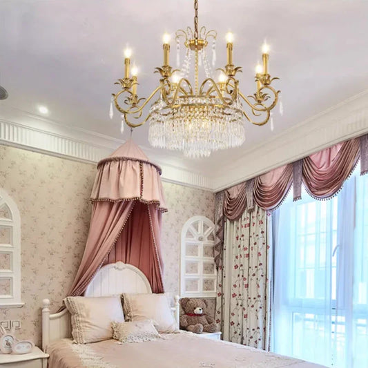 Brass crystal chandelier with pink canopy bed in a bedroom.