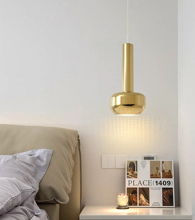 Gold pendant light above a white nightstand with a magazine and candle.