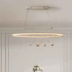 A long, oval-shaped chandelier with multiple rings adorned with clear crystals and hanging butterfly ornaments, suspended from a rectangular ceiling plate.