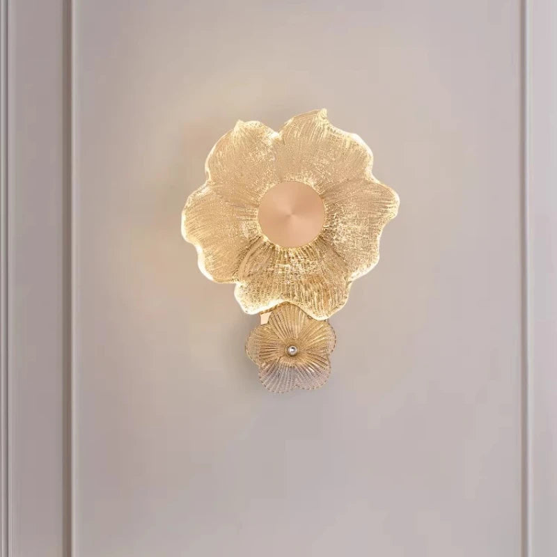 Close-up view of a gold flower-shaped wall sconce, highlighting the textured glass and illuminated petals.