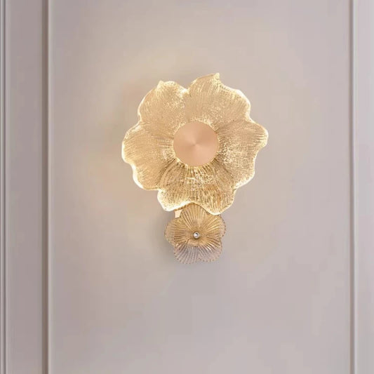 Close-up view of a gold flower-shaped wall sconce, highlighting the textured glass and illuminated petals.