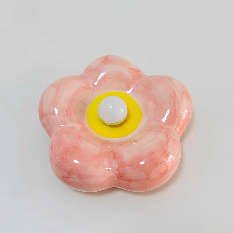 Pink ceramic petal wall sconce with a central yellow accent and white bulb, viewed from the front.