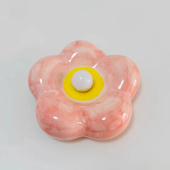 Pink ceramic petal wall sconce with a central yellow accent and white bulb, viewed from the front.