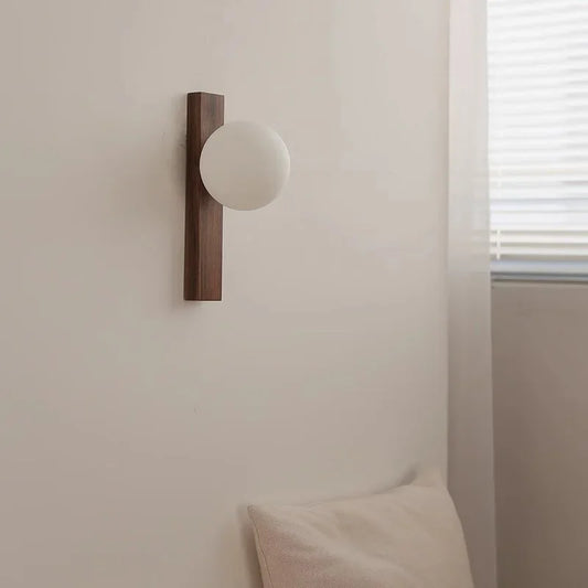 Side view of a modern wood and frosted glass sphere wall sconce, showcasing its clean lines against a white wall and a hint of natural light from a window.